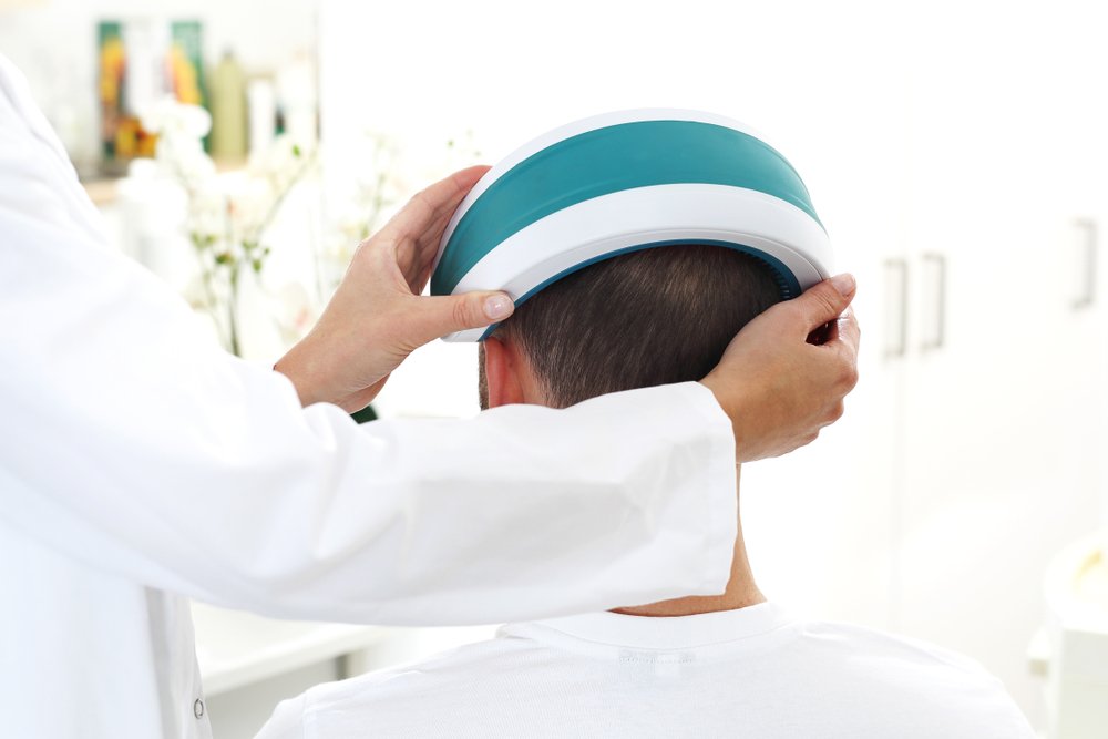 A man has a low level laser hair therapy device placed over his head.