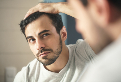 Man looks into mirror and notices his thinning hair.