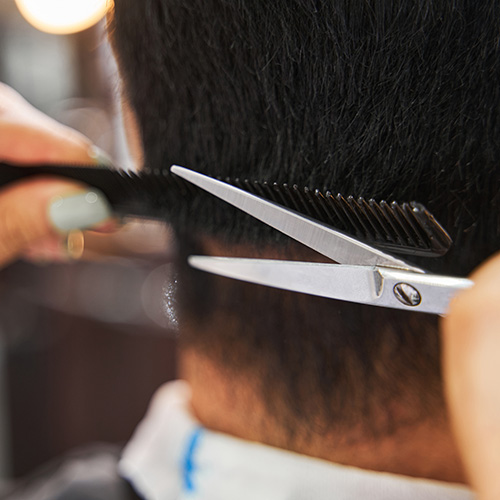Scalp Therapy for Men & Women. A hair stylist uses a comb and scissors to shape the resulting hair from a hair enhancement service.