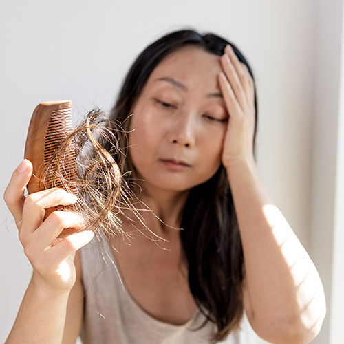 Hair Restoration For Women. A woman looks sadly at the comb full of loose hair in her hand.