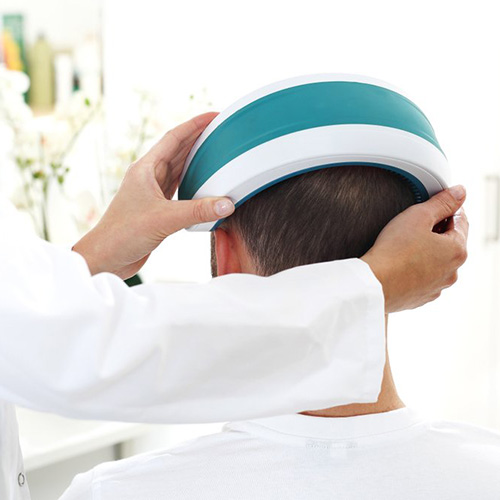 Laser Hair Therapy. A Hair Tech places a laser hair therapy unity over the head of a client.