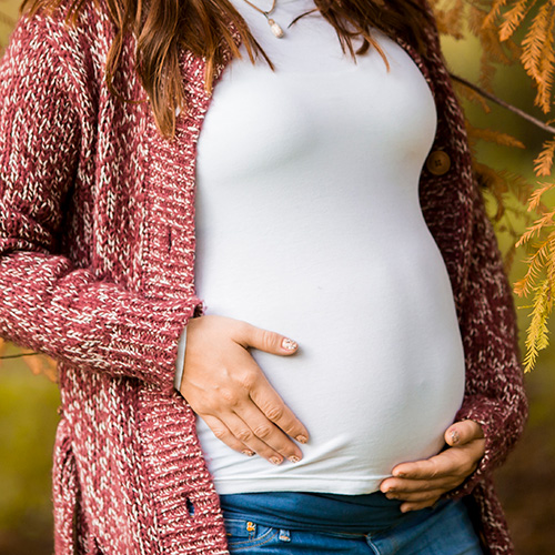 Hair Loss From Pregnancy. A closeup of a woman cradling her pregnant belly.