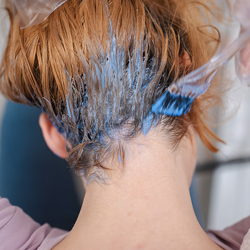 Hair Loss From Hair Styles. A woman brushes dye into the hair at the back of her head.