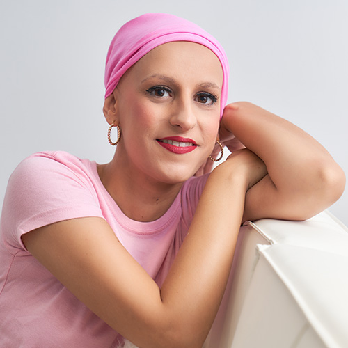 Medical Hair Loss Solutions. A confident woman suffering medical hair loss. She has a bald head that is covered by a pink headscarf.